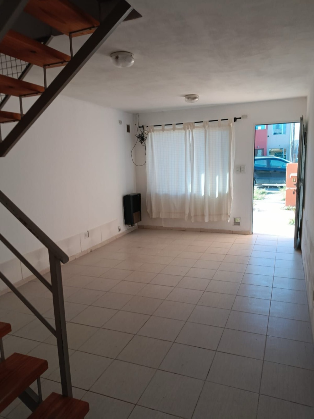 Living con ventana, escalera a la izquierda y la puerta de entrada abierta