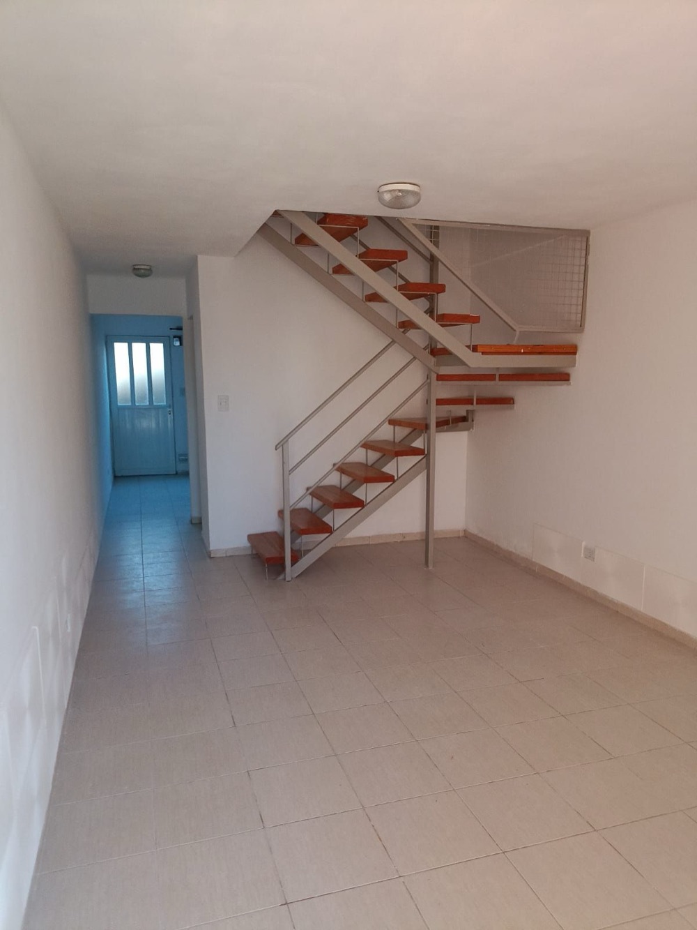 Living comedor con la escalera de madera y hierro y el pasillo hacia el fondo
